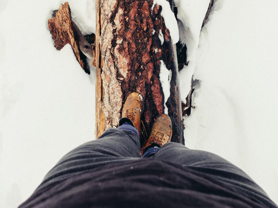 Free Image of Person stands on a snowy log in rugged brown hiking boots 