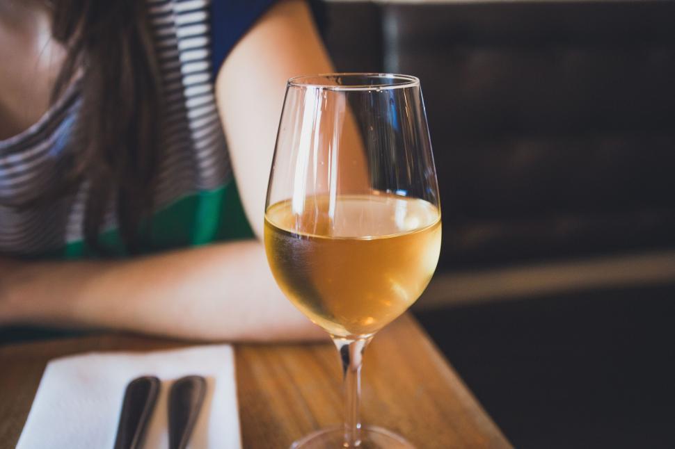 Free Image of Close-up of a glass of white wine on a wooden table inside. 