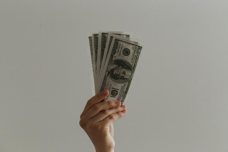 Free Image of Hand holding fanned out dollar bills against plain gray background 