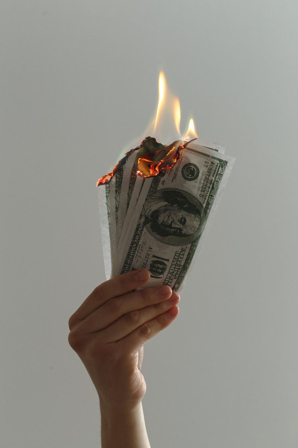 Free Image of Hand held up with burning dollar bills against plain gray background 