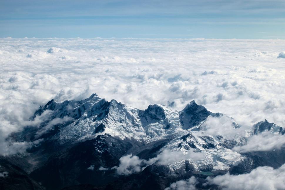 Free Image of Majestic snowy mountain peaks surrounded by clouds viewed from above. 
