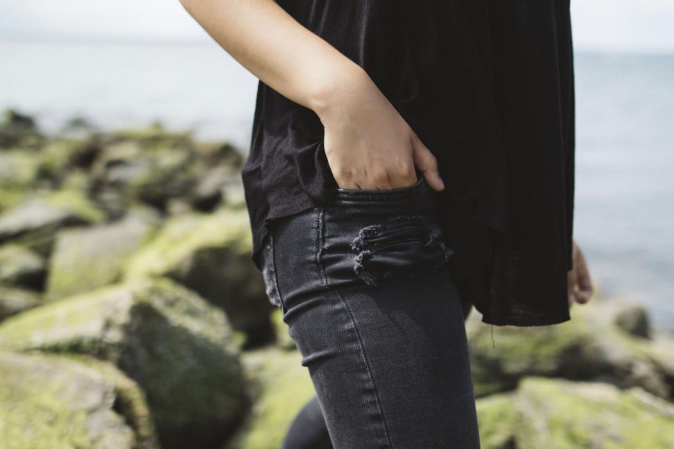 Free Image of Person standing by rocky shoreline wearing black attire, hand in pocket. 