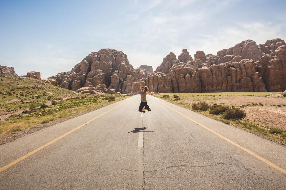 Free Image of Person jumping on a highway with rocky mountains in the background 