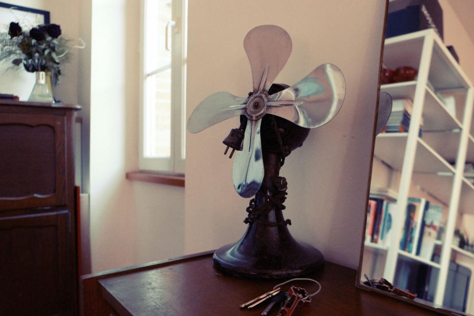 Free Image of Vintage metal fan on wooden table near a brightly lit window. 