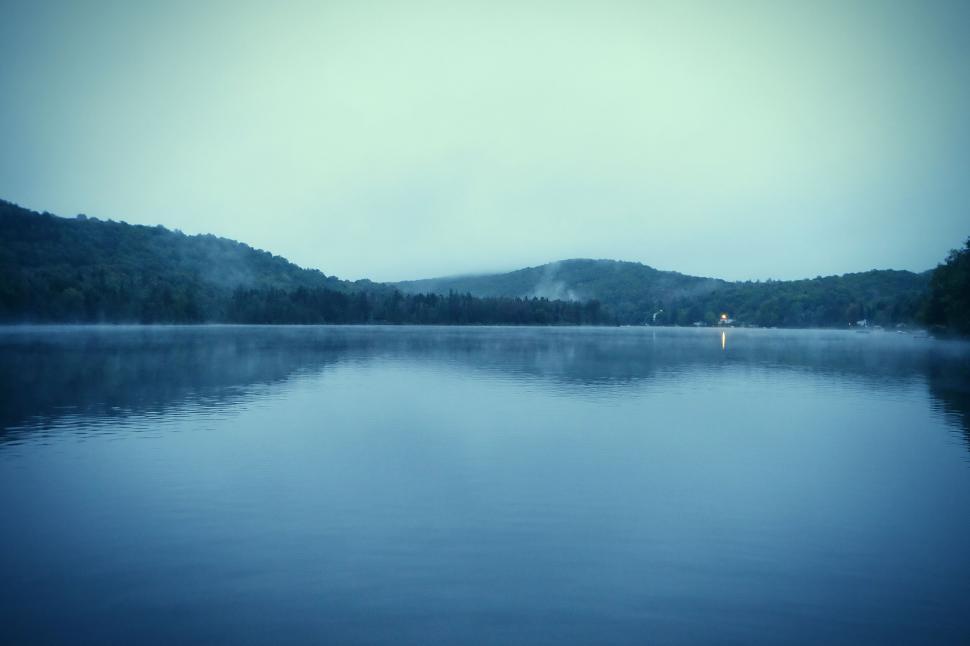 Free Image of A serene lake view at dawn with misty hills in the background. 