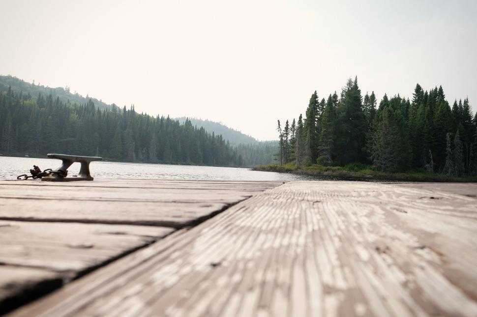 Free Image of Wooden dock extending into calm forest-lined lake scenery. 