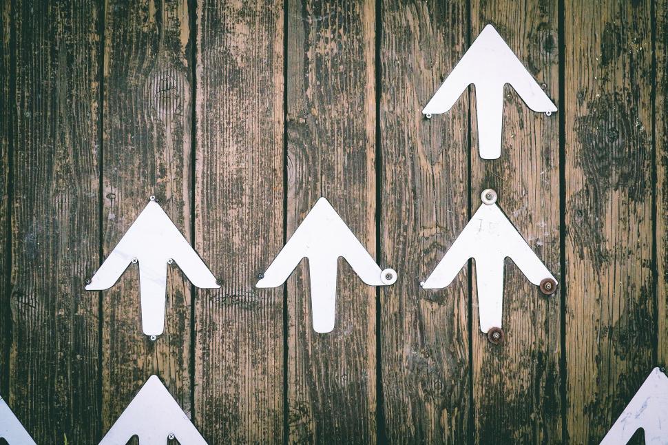 Free Image of White upward arrows on a wooden background symbolizing direction 