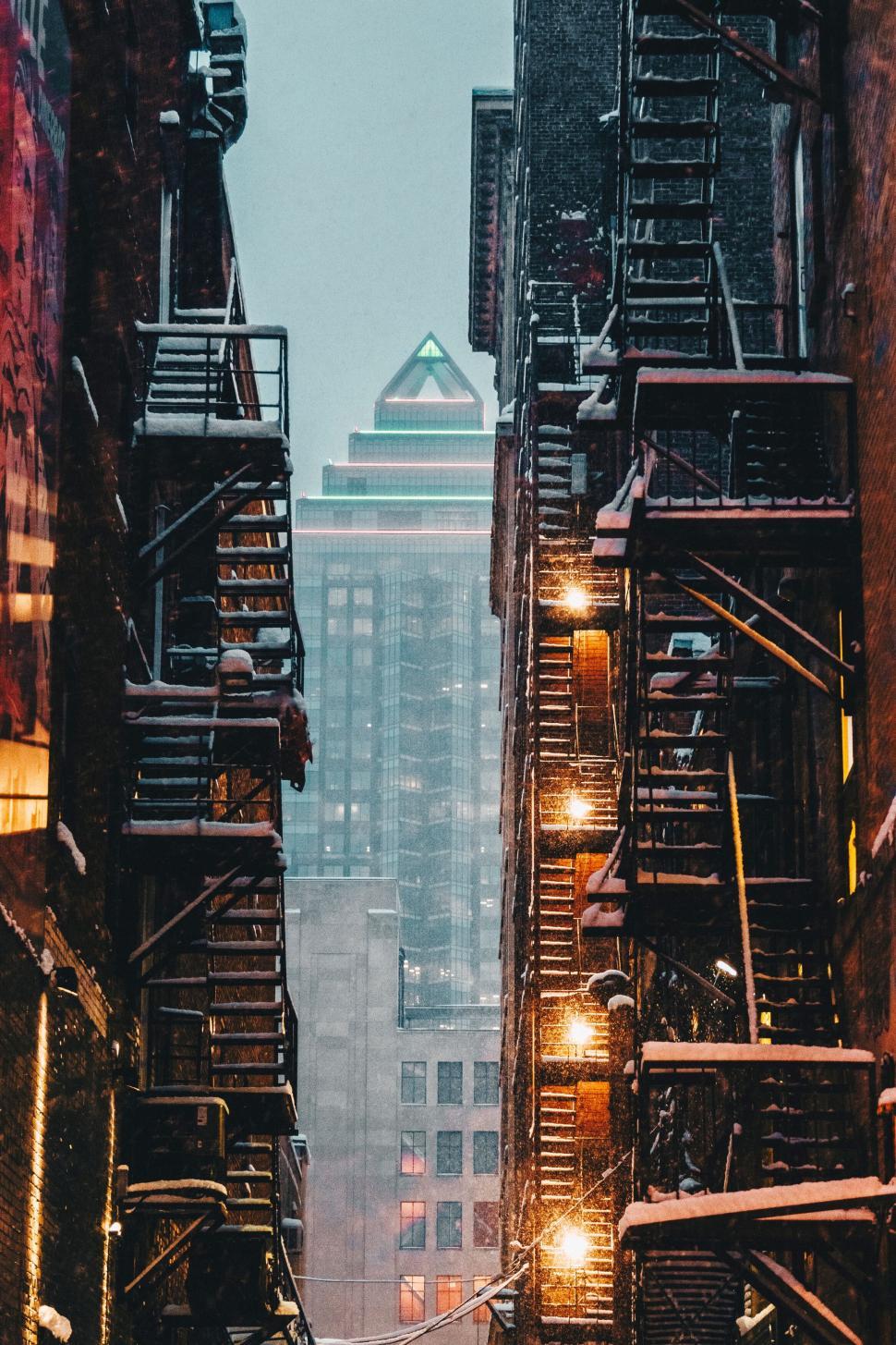 Free Image of City alleyway between buildings with fire escapes and lights on 