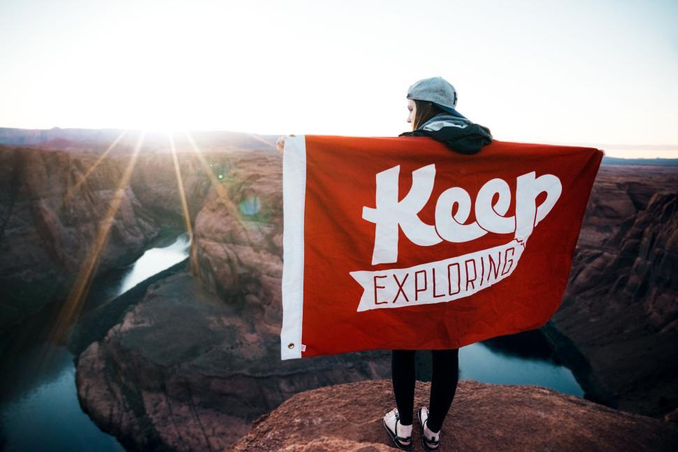 Free Image of Person holding  Keep Exploring  banner atop a cliff with scenic view 