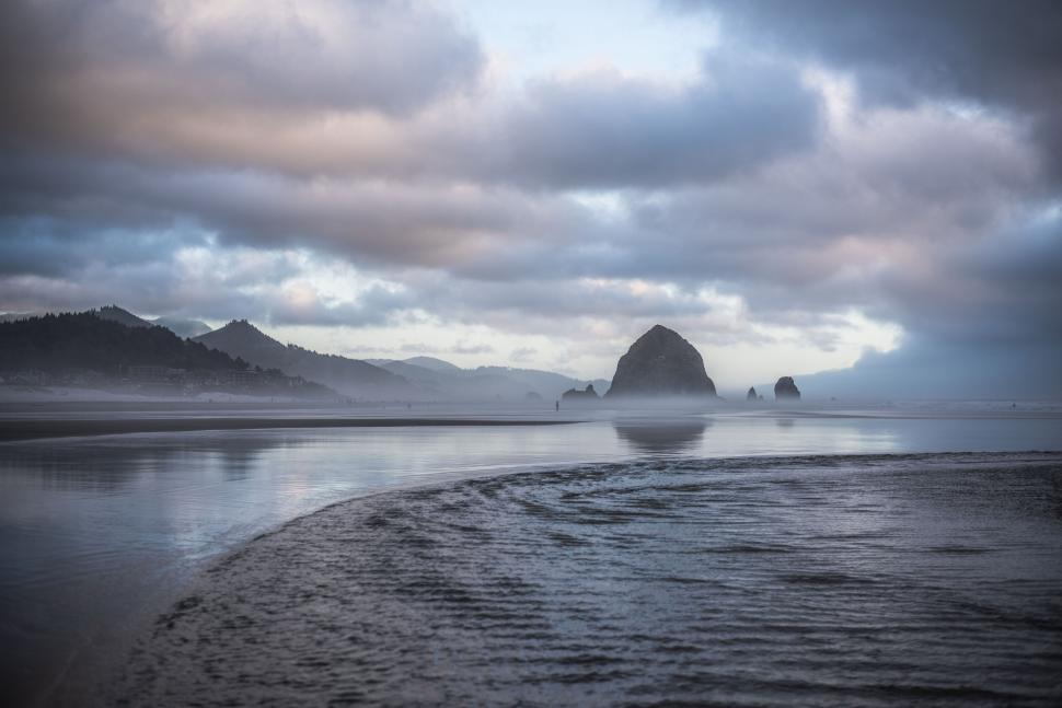 Free Image of Rock formations on a serene beach during a cloudy sunset. 
