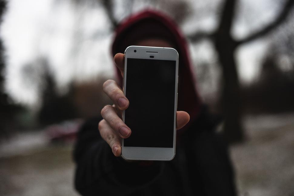 Free Image of Person holding up smartphone with black screen outdoors in park. 