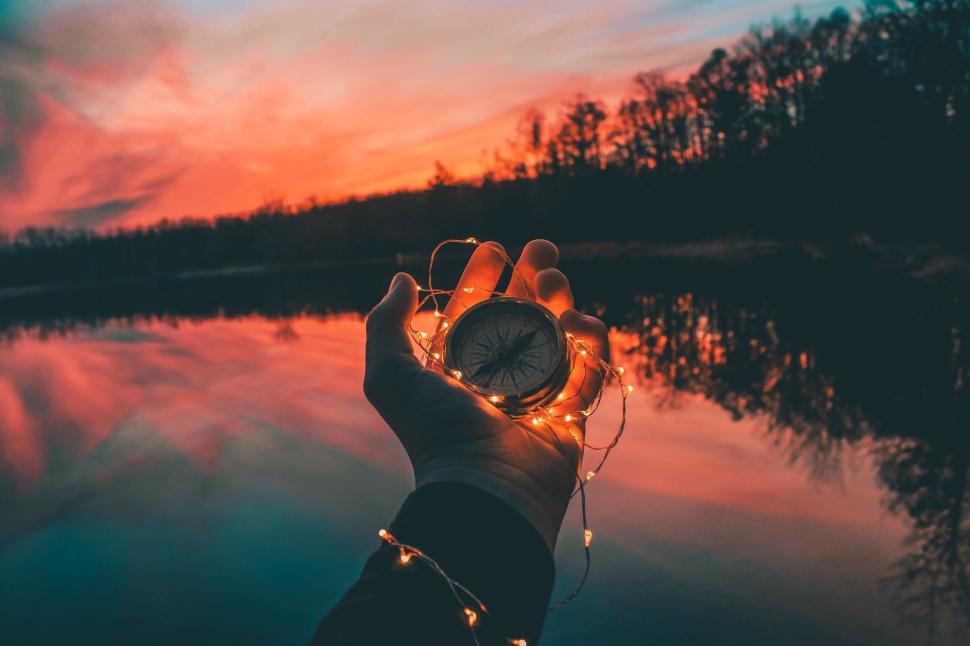 Free Image of Hand holding a compass wrapped in fairy lights at sunset 