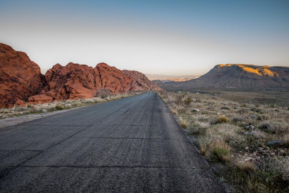 Free Image of Empty highway through vibrant red rocky desert scenery at sunset 