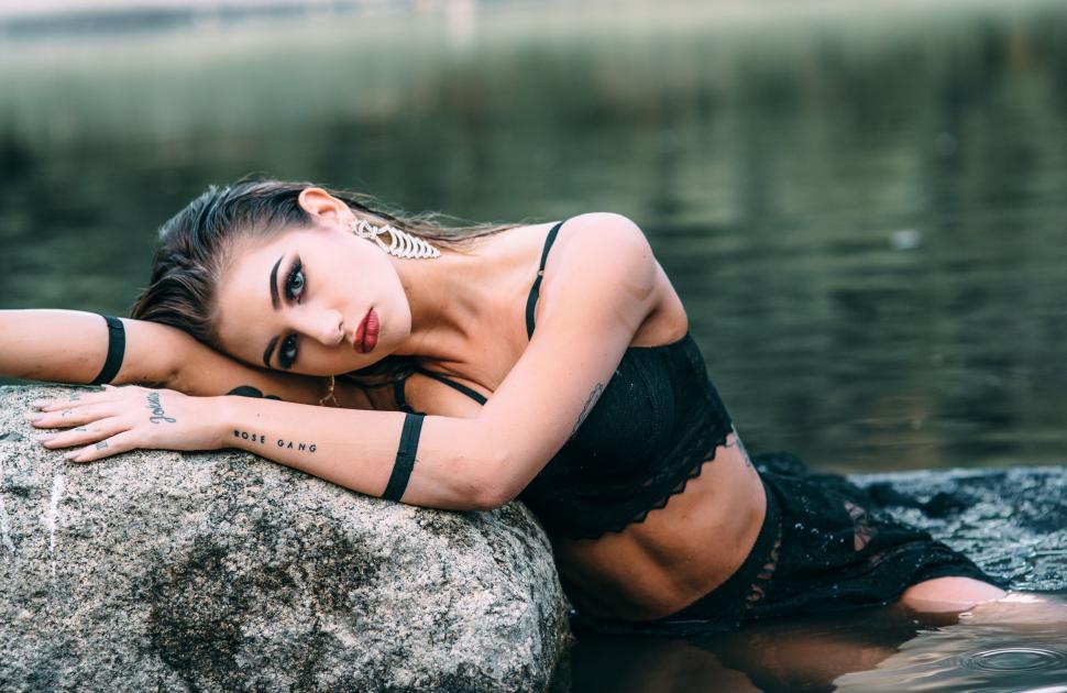 Free Image of Woman in black lingerie posing on rocks at water’s edge of river 
