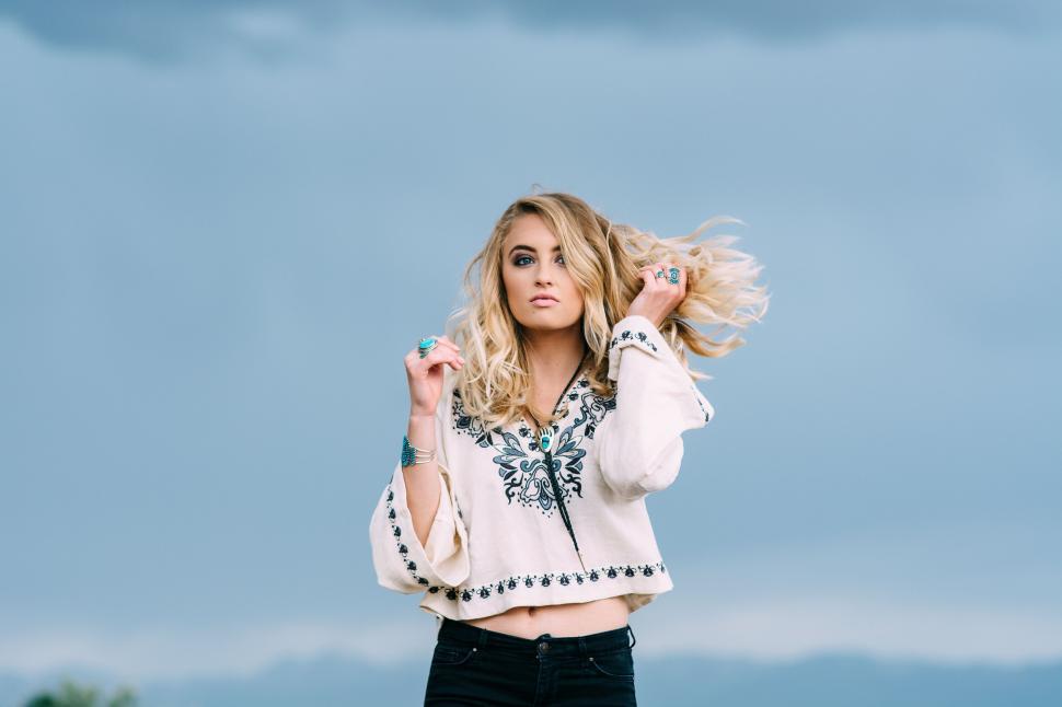 Free Image of Blonde woman with flowing hair posing against cloudy sky 