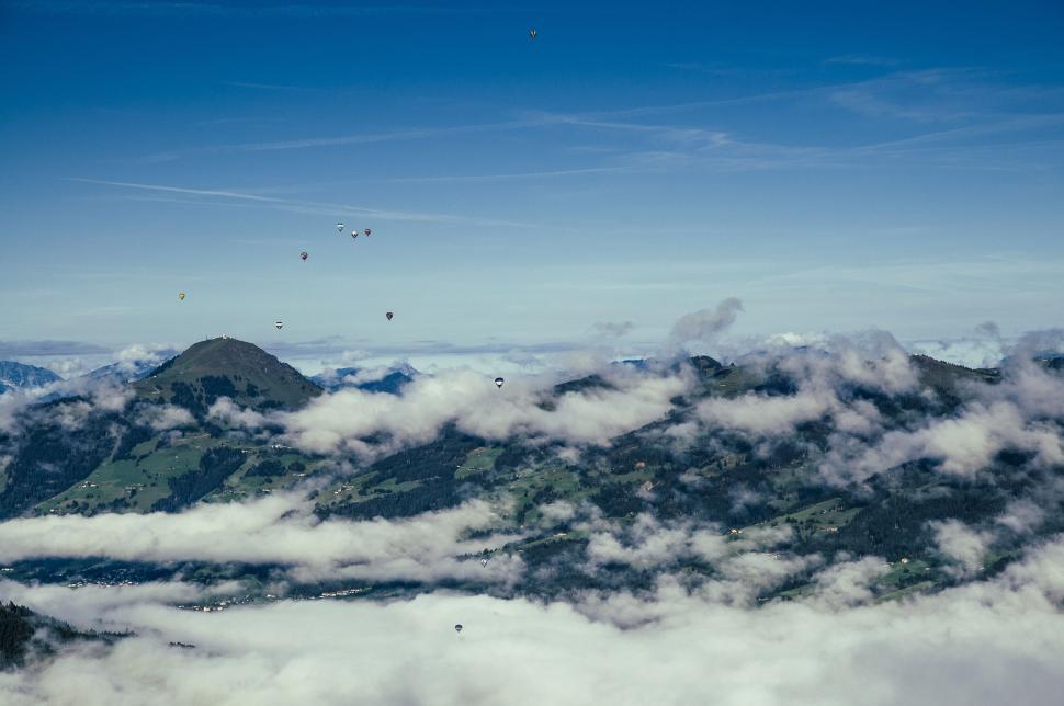 Free Image of Hot air balloons floating over mountains with scattered clouds 