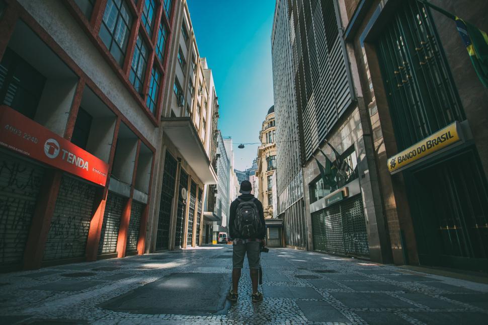 Free Image of Backpacker standing in empty city street between tall buildings. 