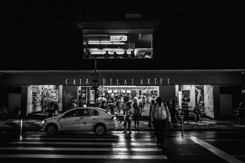 Free Image of Black and white photo of people outside cinema with car crossing. 