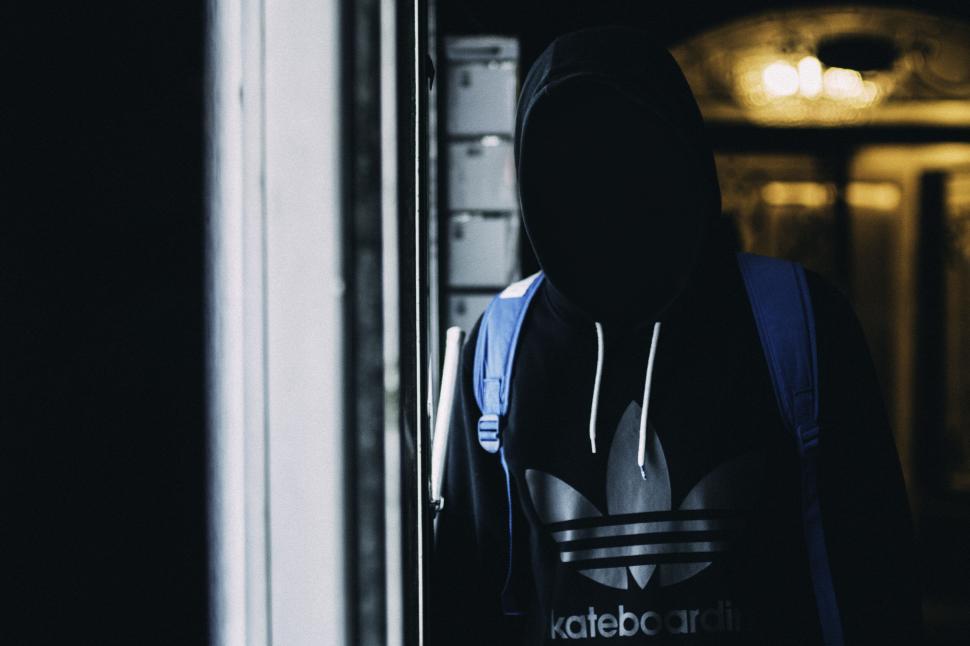 Free Image of Hooded figure in dimly lit interior with blue backpack blending in. 