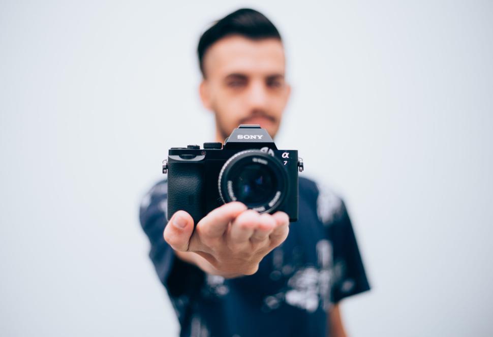 Free Image of Man holding a Sony camera close to the lens, blurred background 
