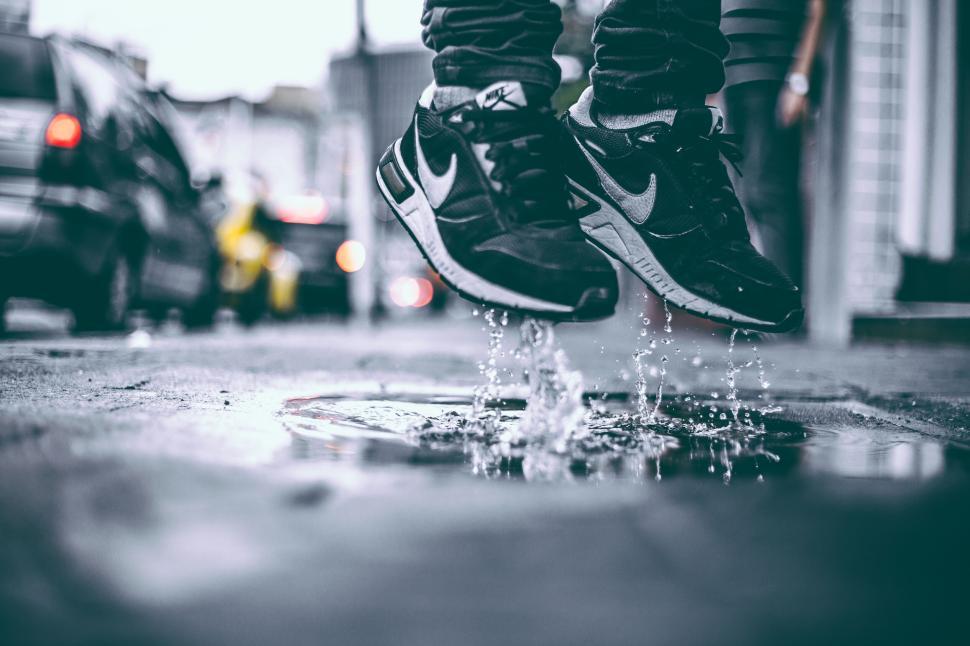 Free Image of Feet in mid-jump splash water in urban street after rainfall. 