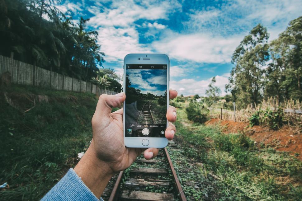 Free Image of Hand holding a smartphone taking a photo of railway tracks. 