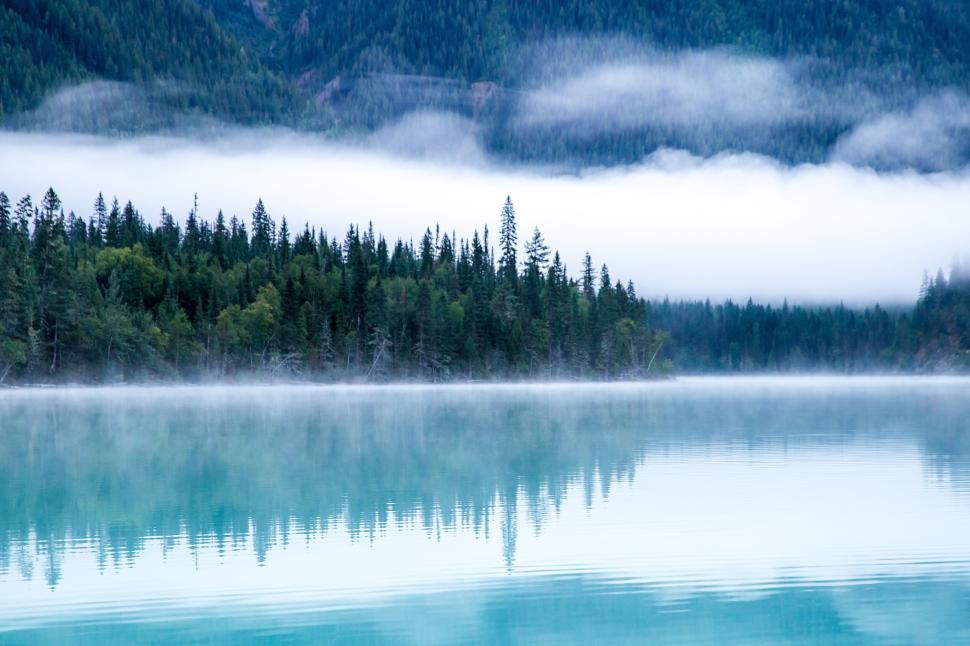Free Image of Pristine turquoise lake reflecting the surrounding forest and mountains. 