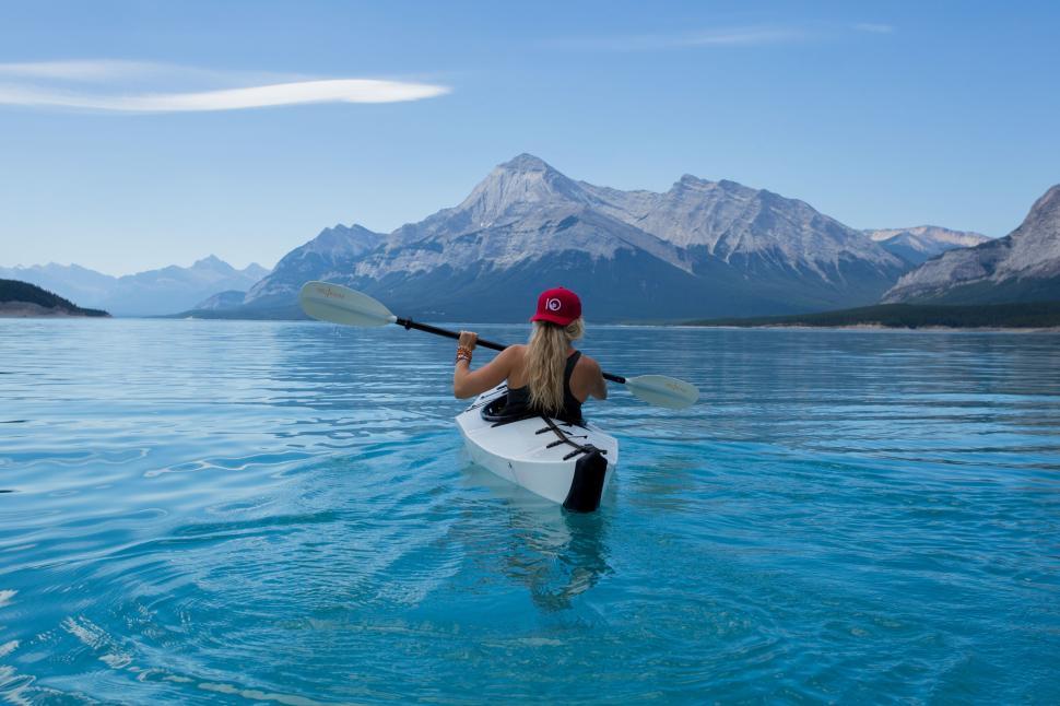 Free Image of Young woman kayaking in clear blue lake with mountains in background. 