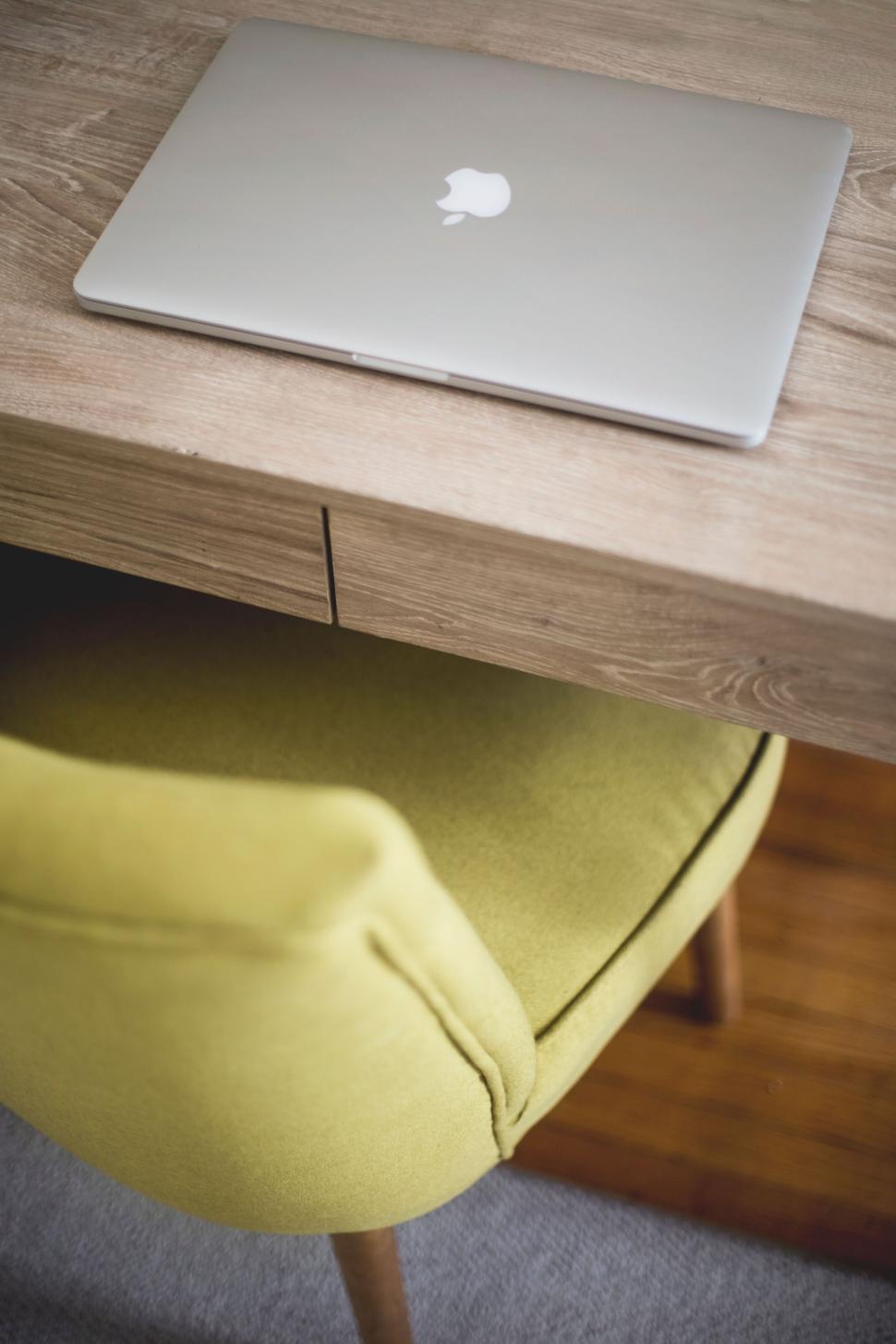 Free Image of Sleek closed laptop on a wooden desk with a lime green chair. 