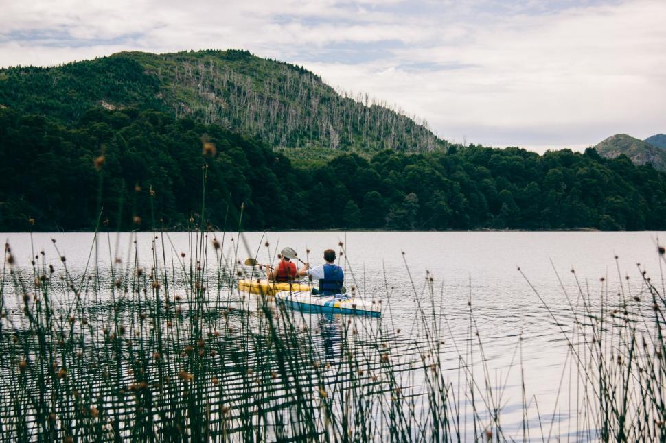 Free Image of Two kayakers paddling on a tranquil lake surrounded by nature 
