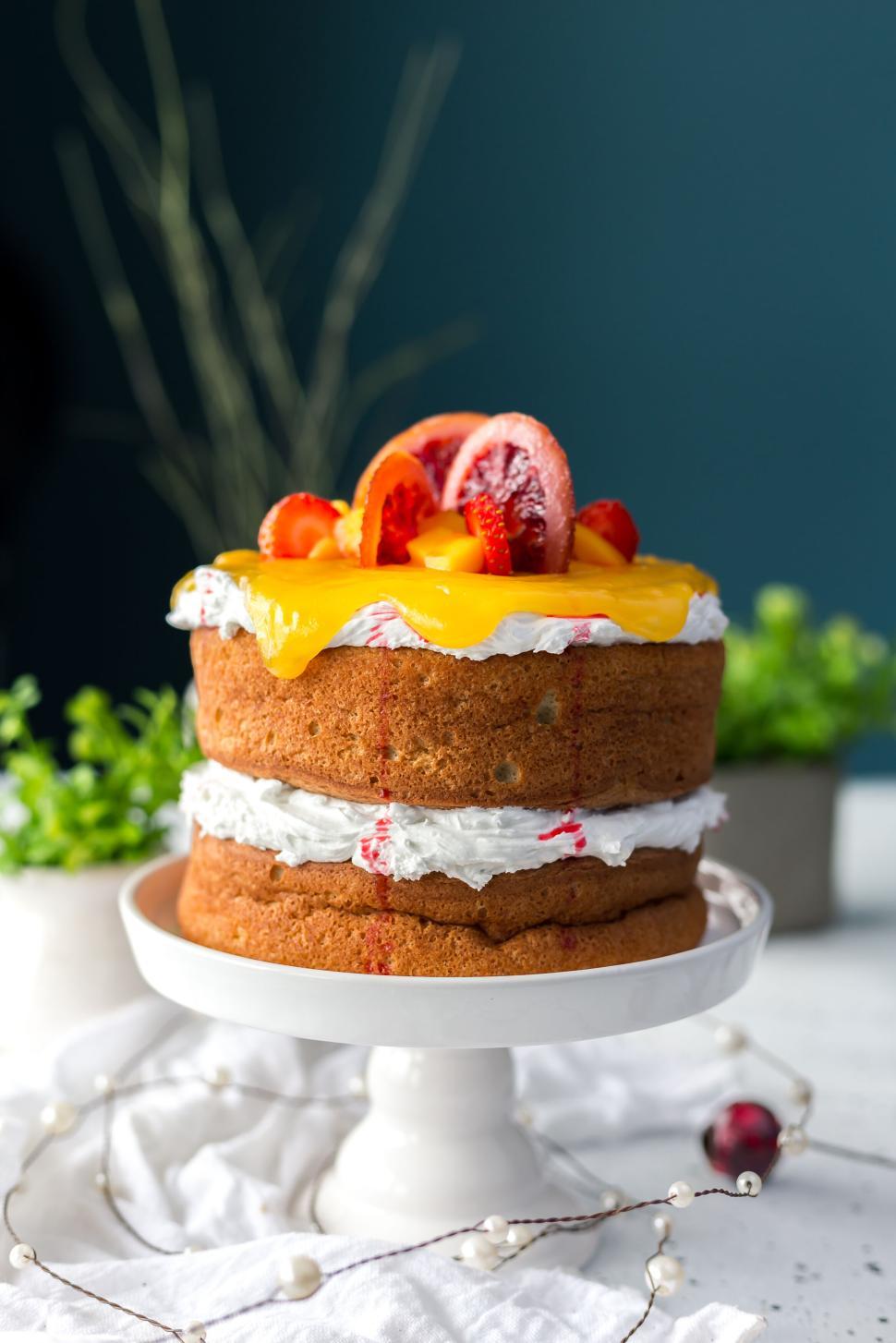 Free Image of Layered cake with fruit toppings and dripping orange glaze 