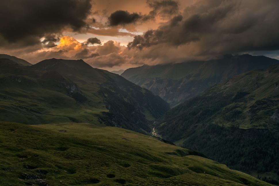 Free Image of Dramatic sunset over mountains with dark clouds and green valleys. 