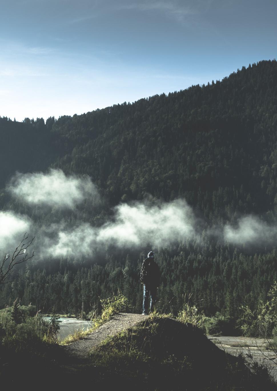 Free Image of Person stands on cliff edge overlooking foggy forest valley. 