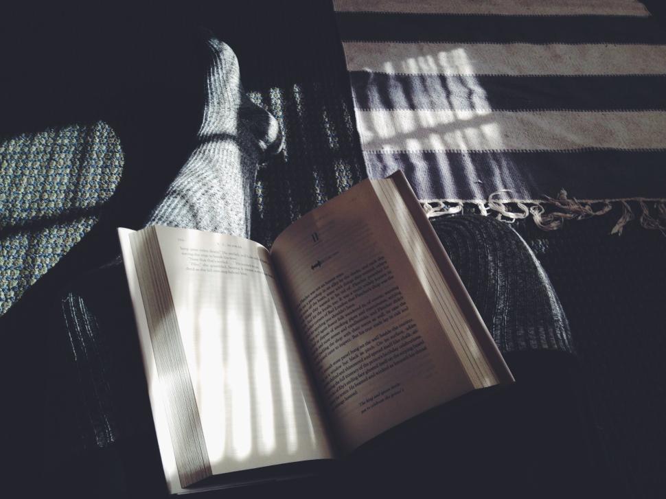 Free Image of Open book on lap with sunlight casting shadows on a cozy home 