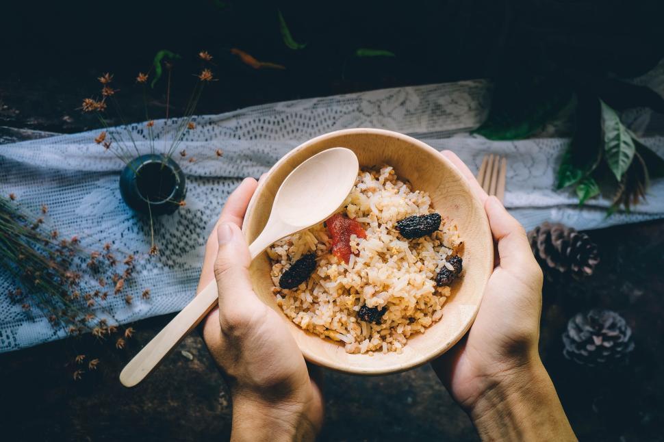 Free Image of Hands holding a bowl of rice with fruit and wooden spoon. 