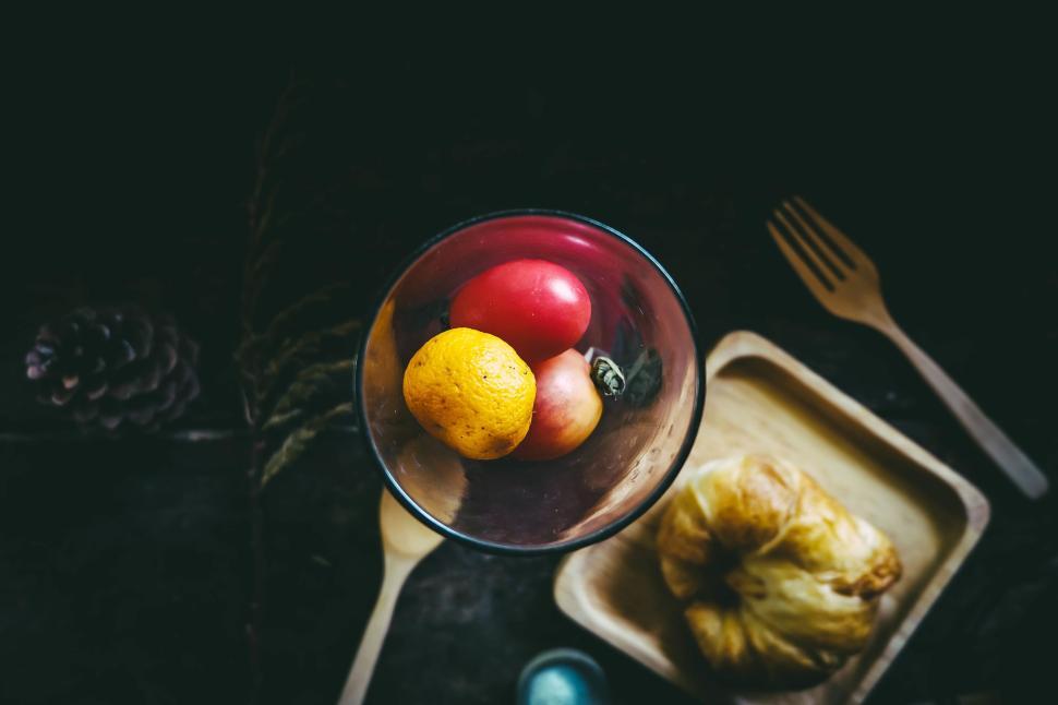 Free Image of A glass vase with fruits and bread on a wooden table setting. 