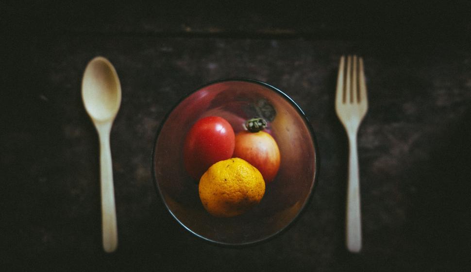 Free Image of Glass vase with small fruits and wooden utensils on dark table. 