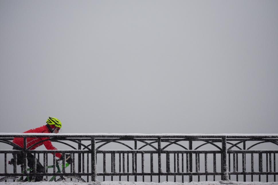 Free Image of Bicyclist in bright gear rides on snowy pathway beside railing 