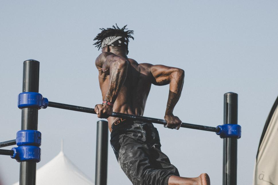Free Image of Muscular man exercising on outdoor workout equipment, mid-movement. 