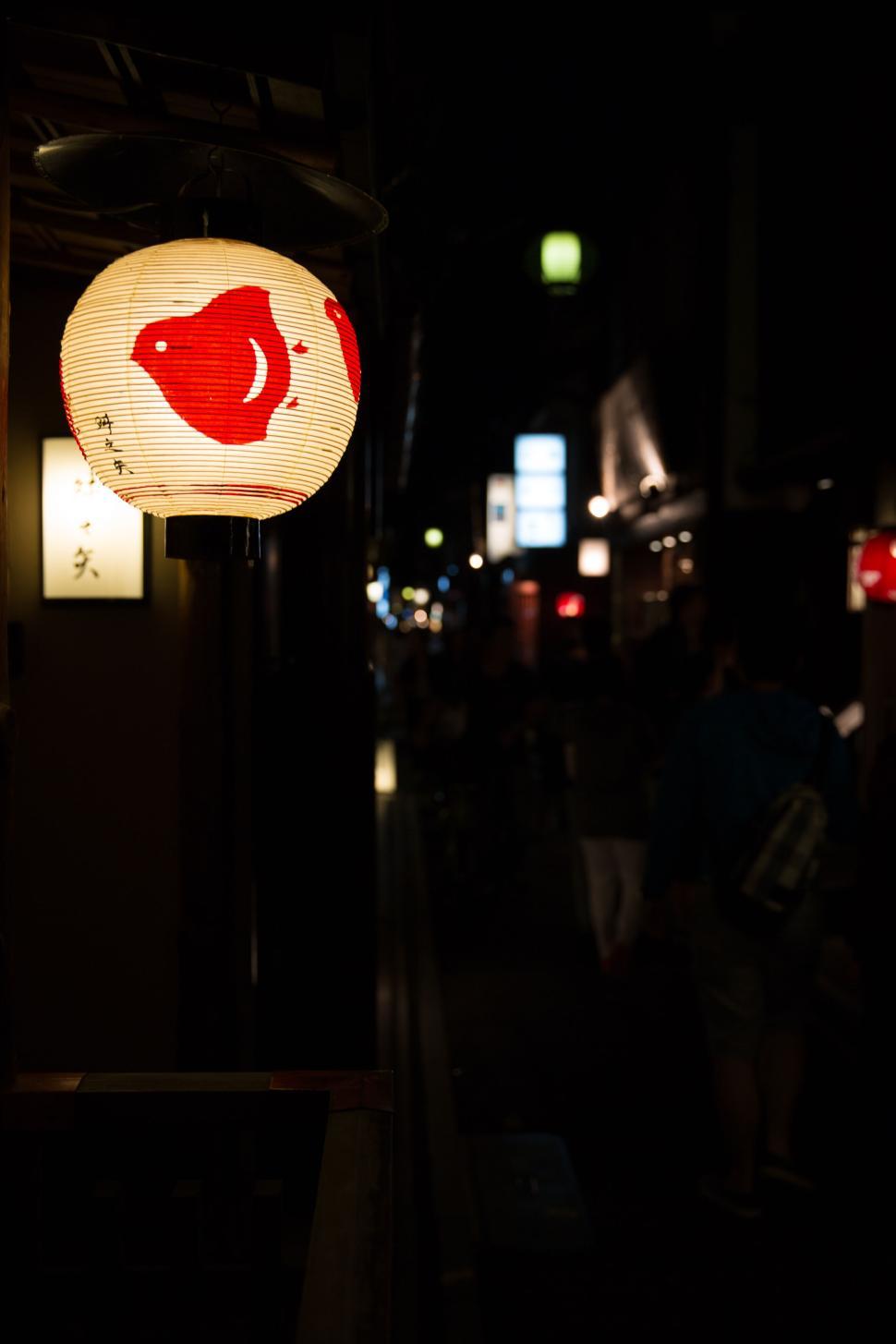 Free Image of Lantern with red fish in nighttime street scene with people 