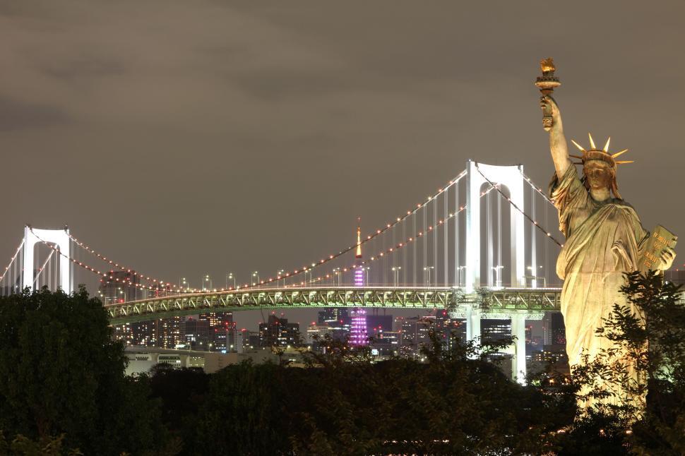 Free Image of Statue of Liberty against bridge and skyline at night in city 