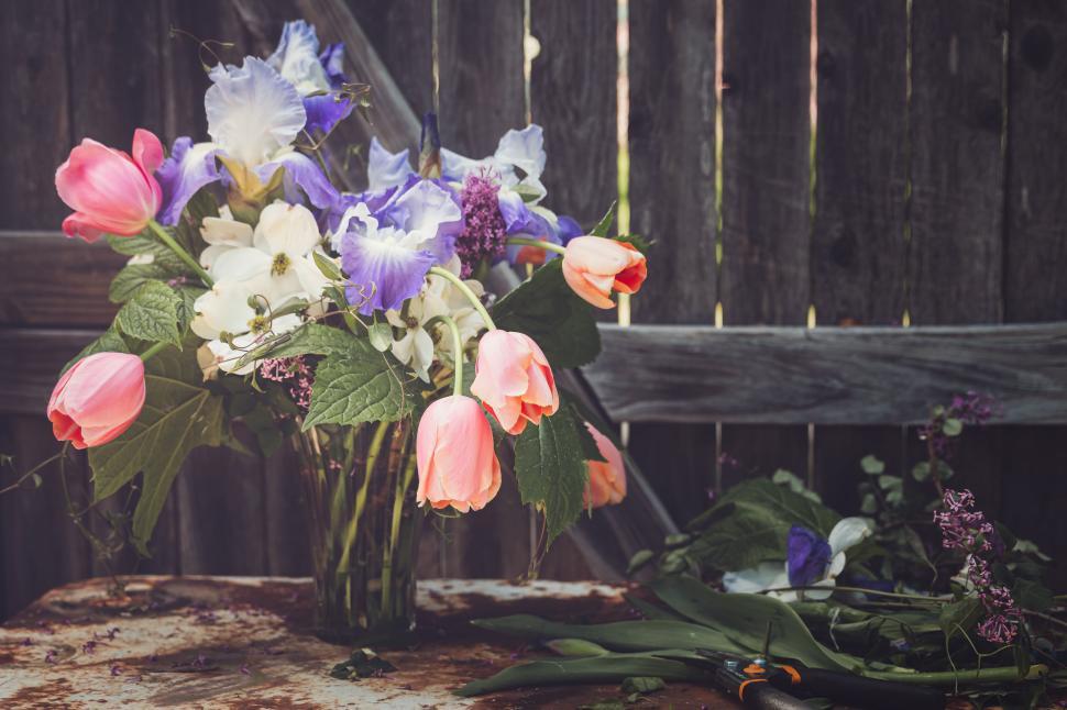 Free Image of A rustic bouquet of assorted flowers in a glass vase outdoors 