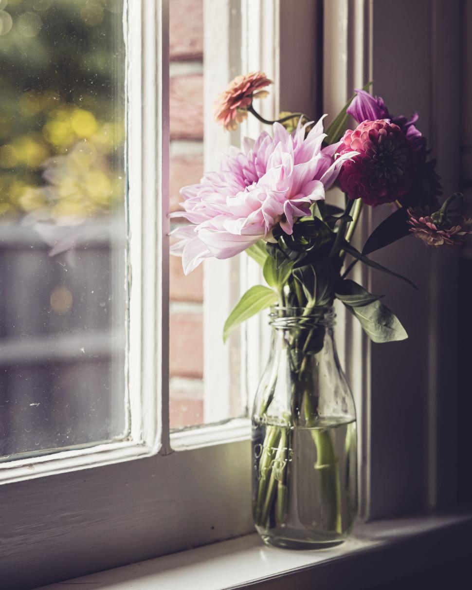 Free Image of Flower Bouquet In Glass Bottle By Sunlit Window With Brick Wall 