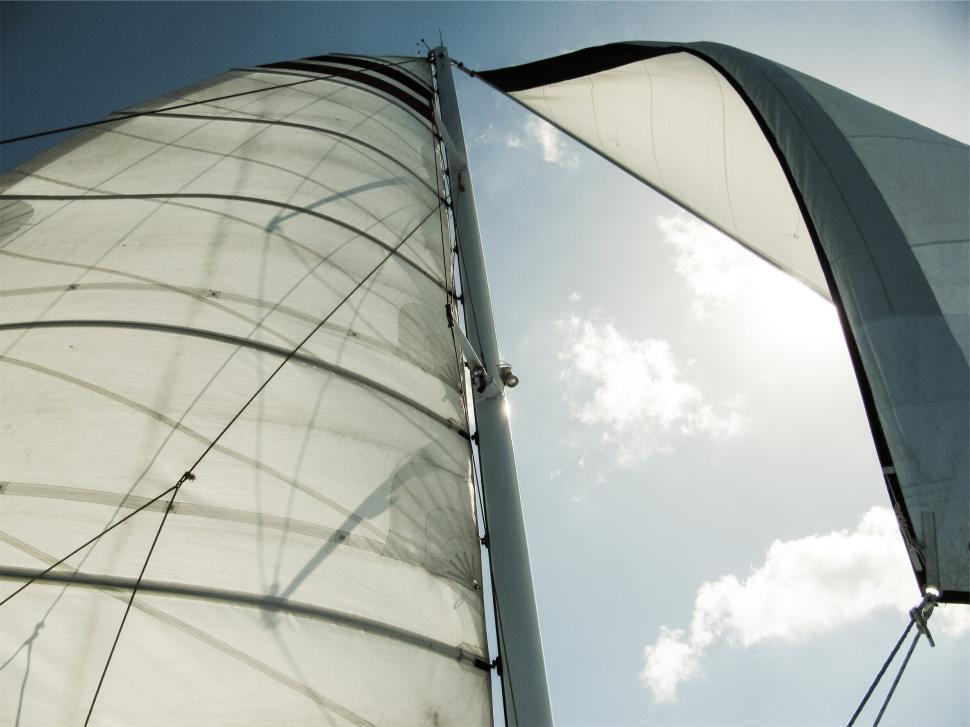 Free Image of Sailboat mast against sky with billowing white sails in sunlight 