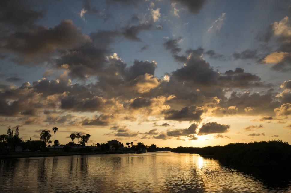 Free Image of Charming waterfront sunset with palm trees and silhouetted clouds 