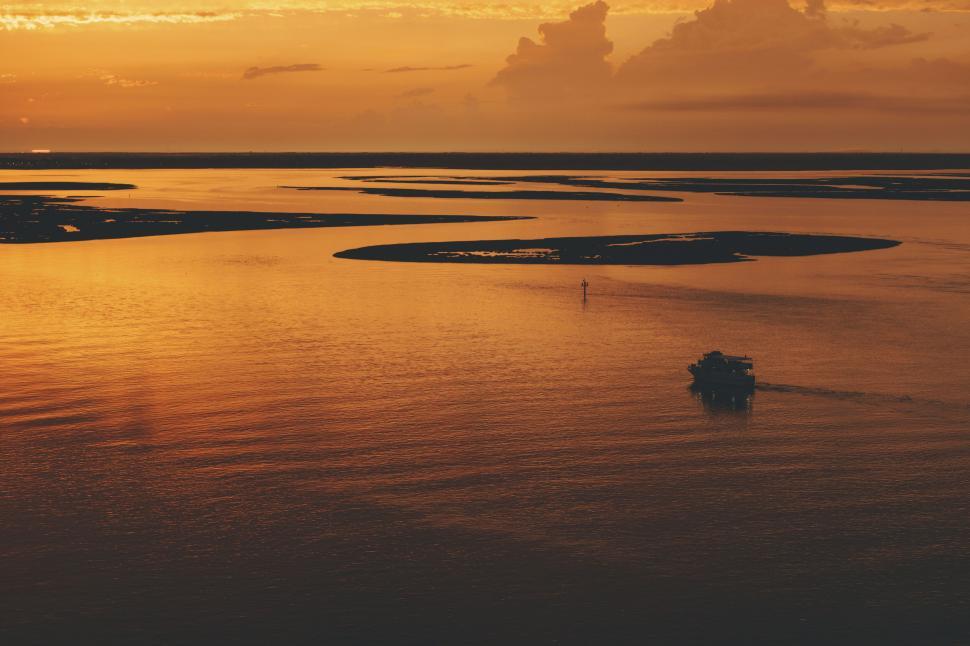 Free Image of Boat sailing on a golden waterway set under a sunset sky. 