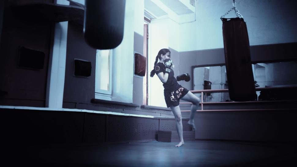 Free Image of Martial artist executing precise movement in gym with punching bags. 