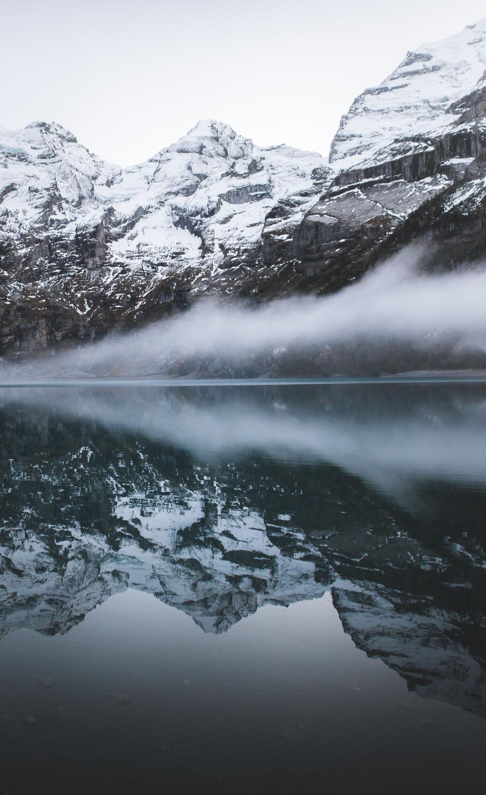 Free Image of Snow-capped mountains reflecting in calm, misty lake waters. 