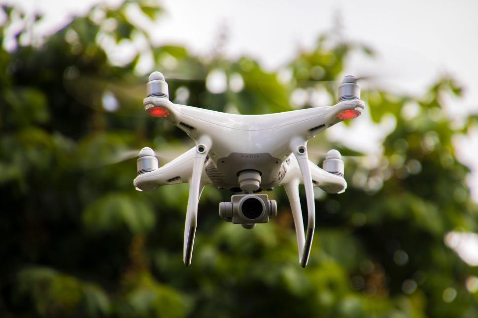 Free Image of White quadcopter drone with camera flying in front of trees 