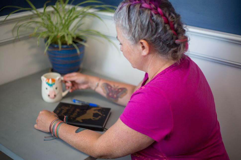 Free Image of Woman with braided hair holding unicorn mug at a table. 